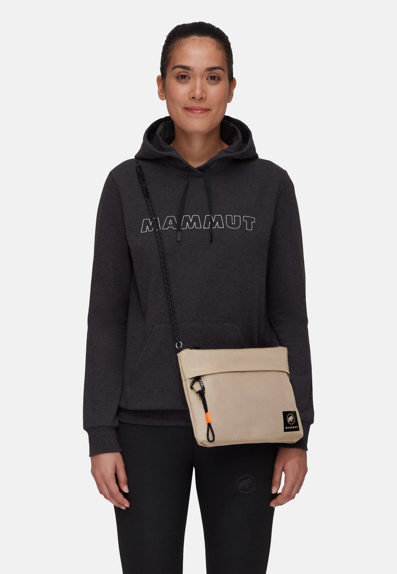 Beige Umhängetasche mit einem umklappbaren Deckel, schwarzem Riemen und orangefarbigen Akzenten. Hergestellt aus strapazierfähigem Material, mit einem Logo-Patch und einem Reißverschluss.