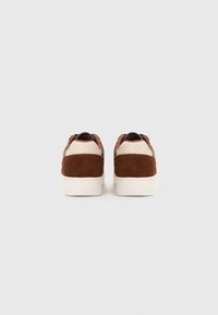 Braune Wildledersneaker mit einer cremefarbenen Lederferse und schwarzen Akzenten. Sie haben eine weiße Gummisohle und ein klassisches Low-Top-Design.