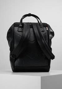 Mochila negra de cuero con correas de hombro ajustables duales, un asa en la parte superior, acentos acolchados y cierre con cremallera.