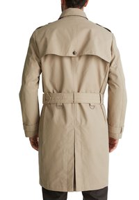 Trench-coat beige avec un design croisé, une fente au dos, une taille ceinturée et des épaulettes boutonnées. Texture lisse, longueur genou.