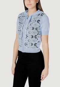 Cárdigan de cremallera azul claro con diseño de encaje en la parte delantera, mangas cortas y capucha. Los detalles en negro del encaje crean un patrón floral.