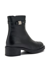 Bota al tobillo de cuero negro con puntera redonda, tacón ancho de altura media y adorno de hebilla exterior. Textura lisa con detalles sutiles de costura.