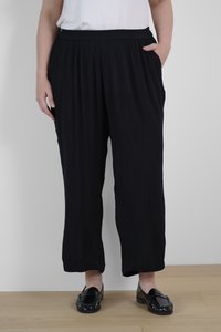 Schwarze, locker sitzende Hose mit Gummibund, aus strukturiertem Stoff und Seitentaschen. Kombiniert mit glänzenden schwarzen Slippern.