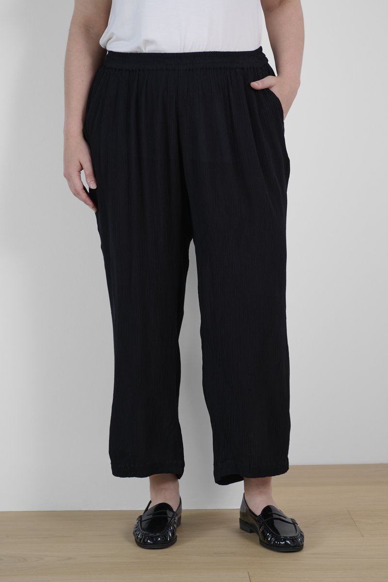 Black, loose-fitting pants with an elastic waistband, featuring a textured fabric and side pockets. Paired with glossy black loafers.