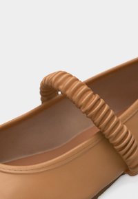 Ταν επίπεδο παπούτσι με υφασμάτινο ελαστικό λουράκι στην κορυφή και λεία, στρογγυλεμένα άκρα.