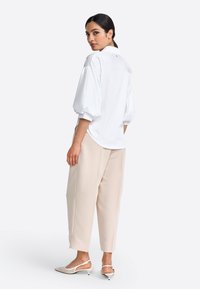 Weißes Blusenoberteil mit Ballonärmeln und hohem Kragen, kombiniert mit beigen, schmal zulaufenden Hosen und cremefarbenen Slingback-Schuhen. Aus glattem Stoff und mit lässiger Passform.