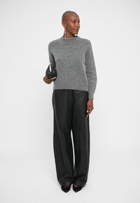 Maglione grigio di lana con collo alto, abbinato a pantaloni larghi in pelle nera e una piccola borsa nera. Orecchini semplici aggiungono un tocco di dettaglio.