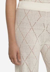 Stickade leggings i mjuk beige med ett diamantmönster. Har en bred elastisk midja och en strukturerad öppen väv. Hand synlig på sidan.