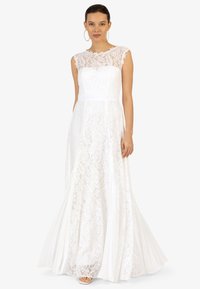 Robe sans manches en dentelle blanche avec un corsage ajusté et une jupe fluide. Présente un col en dentelle festonné et une ceinture lisse.