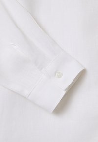 Puño de camisa de lino blanco con un cierre de un solo botón, que presenta una textura suave y un sutil patrón tejido.