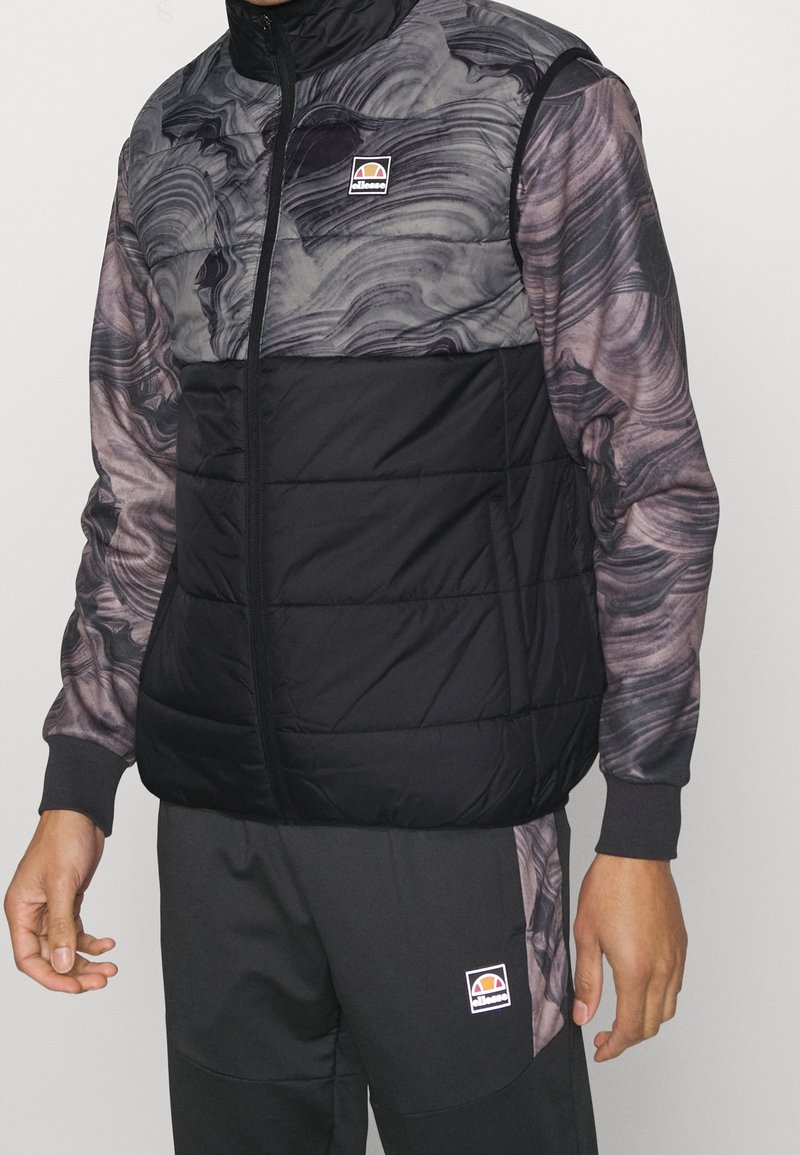 Vadderad väst med svart quiltad nederdel och grå marmorliknande mönster på övre delen, med hög krage och logotypmärke på bröstet.