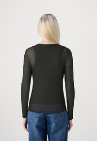 Långärmad svart topp i genomskinligt material, med rund halsringning och en figurnära silhuett. Kombinerad med blå högmidjade jeans.