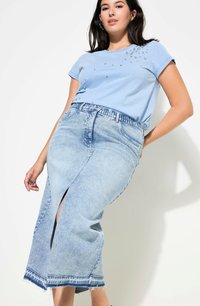 Top de manga corta azul claro con detalles decorativos, combinado con una falda de mezclilla de tiro alto y abertura en un lavado claro con dobladillo deshilachado.