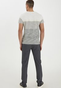 Grå og hvid stribet kortærmet t-shirt med rund hals, parret med mørkegrå sweatpants og sorte sneakers, set fra bagved.
