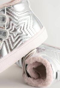 Silberne High-Top-Sneakers mit einem strukturierten Zickzackmuster, ausgestattet mit einem weichen, rosa Kunstfellfutter und zwei Klettverschlüssen zur Befestigung.