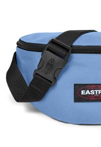 Modrá nylonová ledvinka má černý nastavitelný popruh, plastovou sponu a zipové zavírání. Značka je zobrazena na černé nášivce.