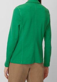Zelená bunda s dlouhým rukávem, přiléhavého střihu, hladké textury a límcem. Má jemné švy a rovný lem.