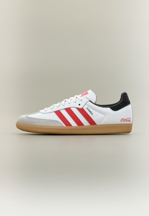 Biały sneaker Adidas Samba z czerwonymi paskami, gumową podeszwą, czarnym obcasem i logo Coca-Cola z boku.