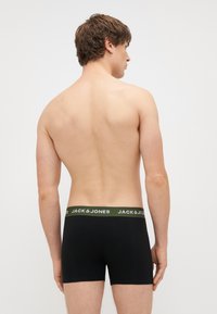 Μαύρα μποξεράκια με πράσινη ελαστική μέση που φέρουν την επιγραφή "JACK & JONES" σε λευκό χρώμα, φορεμένα από ένα άτομο που είναι στραμμένο προς τα πίσω, δείχνοντας το πίσω προφίλ.