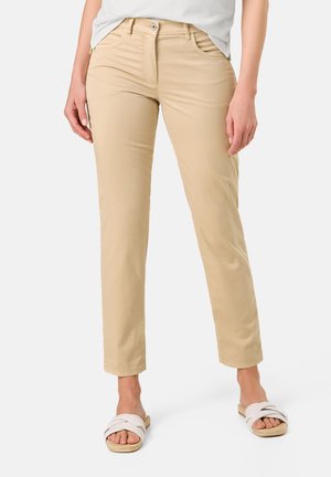 Beige straight-leg pants with front pockets, a zipper fly, and contrasting stitching. Worn with light-colored, cross-strap slide sandals.