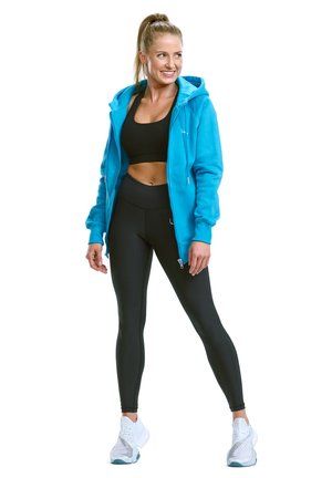 A turquoise fleece zip-up hoodie, black crop top, and black leggings, paired with white athletic shoes, showcasing a fitted design.