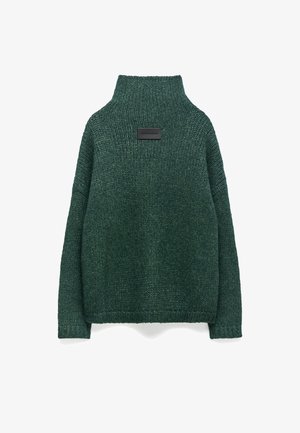 Donkergroene gebreide trui met een hoge kraag, losse pasvorm, verlaagde schouders en een rechthoekige patch op de rug met reliëftekst.