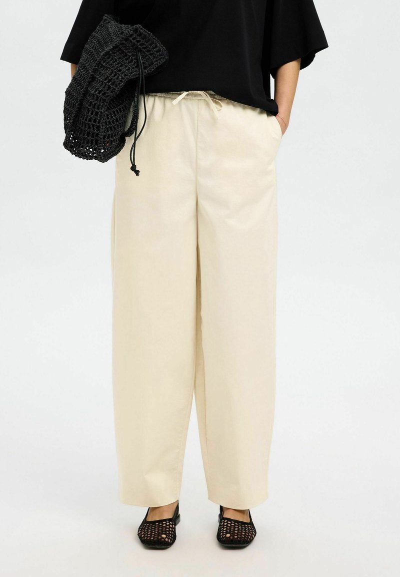 Pantalons larges cream avec une taille élastique, associés à un sac à main en crochet noir. Les chaussures présentent un motif en maille noir.