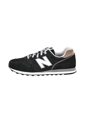Zapatilla New Balance en blanco y negro con cordones grises, paneles de malla y ante, lengüeta trasera marrón y suela de goma sobre fondo blanco.
