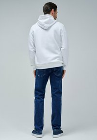 Sudadera blanca con capucha, jeans de mezclilla azules, zapatillas deportivas grises. Se enfoca en colores sólidos y un diseño simple, con costuras visibles y detalles en los bolsillos.