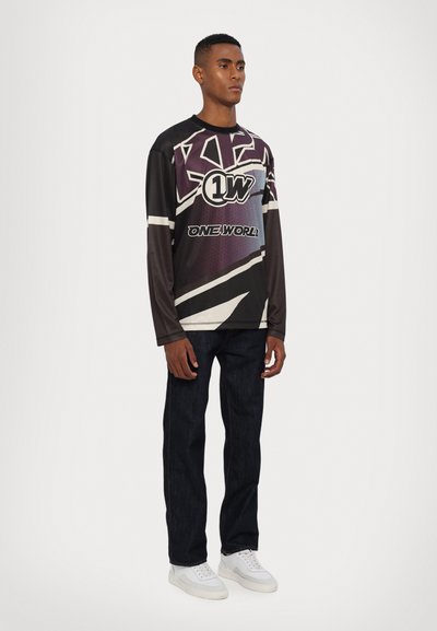 Langarmshirt mit grafischem Design in Schwarz, Lila und Weiß. Kombiniert mit dunklen Jeans und weißen Sneakers.