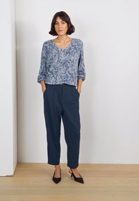 Blouse bleue à motifs floraux avec des manches trois-quarts. Pantalon bleu marine, fuselé avec une coupe décontractée. Talons noirs à bout pointu.