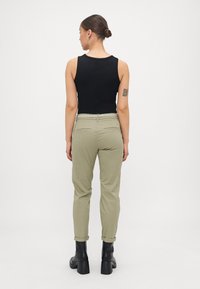 Top preto sem mangas combinado com calças verdes oliva ajustadas, apresentando uma bainha rolada. Usado com botas de cano curto pretas com salto. Vista traseira.