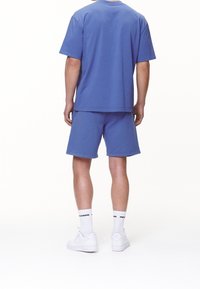 Ensemble t-shirt et short en coton bleu, coupe décontractée, design uni, vue de dos, avec des baskets blanches et des chaussettes ornées de texte noir.