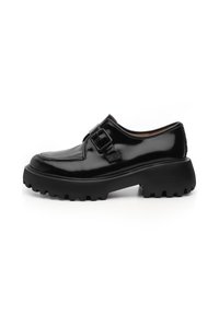Zapato de charol negro con punta redonda, que presenta un hebilla lateral y una suela de goma gruesa y texturada. Acabado suave con un diseño elegante.