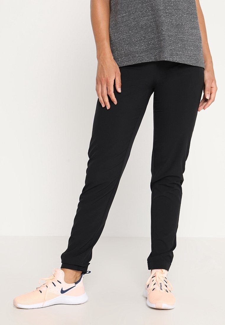 Černé sportovní kalhoty vyrobené z lehkého materiálu. Zúžený střih s elastickými manžetami, doplněné o světle růžové boty s tmavě modrým logem.