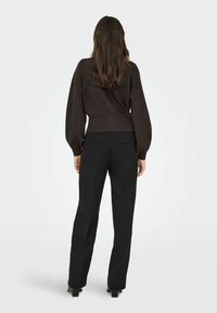 Black tailored trousers and a cropped dark brown sweater with puffed sleeves. The fabric appears soft, and the outfit features a clean, modern design.