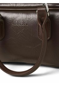 Nahaufnahme einer dunkelbraunen Ledertasche mit strukturierter Oberfläche, robustem Griff, Metallbeschlägen und eingeprägtem "JJXX"-Logo auf der Vorderseite.