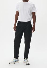 Svarta byxor med en slät yta och skräddarsydd passform, kombinerat med en vit t-shirt med rund hals och silvriga träningsskor.