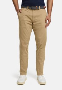 Khaki cotton chinos with a straight fit, featuring side pockets, a navy and white patterned belt, and worn with white sneakers.