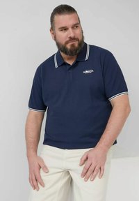 Dunkelblaues Polohemd mit weißen Streifen am Kragen und an den Ärmeln, mit einem kleinen Logo auf der linken Brust. Aus Baumwollstoff, entspannte Passform.