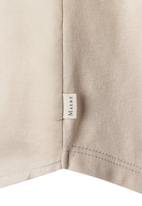 Tela beige con dos texturas de punto diferentes unidas por una costura, con una pequeña etiqueta blanca con "MAERZ" impresa verticalmente.