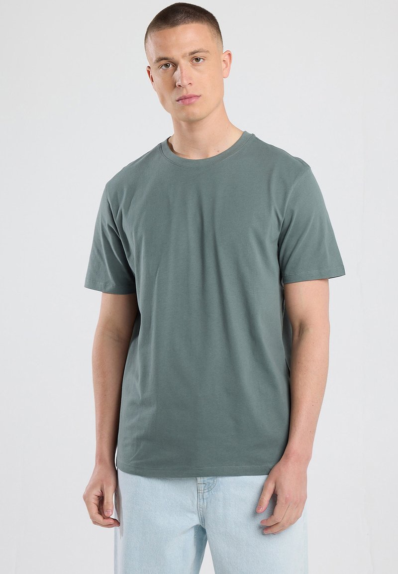 Short-sleeve, crew-neck t-shirt in olive green cotton, featuring a relaxed fit and smooth texture. Worn with light blue jeans.
