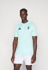 Mint green athletic shirt with black Adidas logo and Juventus emblem, accented by yellow and pink detailing. Worn with white shorts.