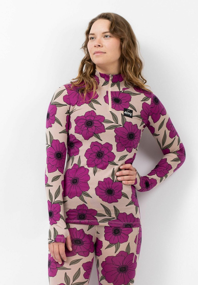 Long-sleeve, zippered top in light beige with large purple floral print and green leaves. Includes a small black logo patch on the chest.