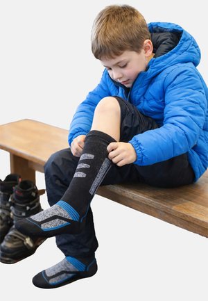 Black and gray textured socks with blue accents, featuring a zigzag pattern, worn by a child sitting on a wooden bench.