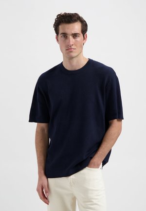 Navyblauwe, geribbelde t-shirt met korte mouwen en een ronde hals, gedragen met lichtgekleurde broeken; casual pasvorm en gestructureerd oppervlak.