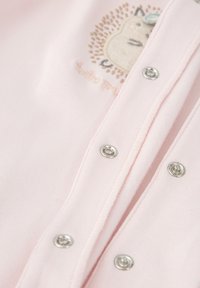 Prenda de color rosa claro que presenta cierres a presión, fabricada en algodón suave, y con un diseño bordado de un erizo con detalles sutiles.