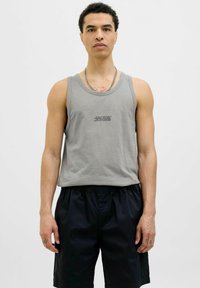 Camiseta de algodón gris sin mangas con cuello redondo y un pequeño logo negro centrado en el pecho, combinada con pantalones cortos negros. Textura suave.