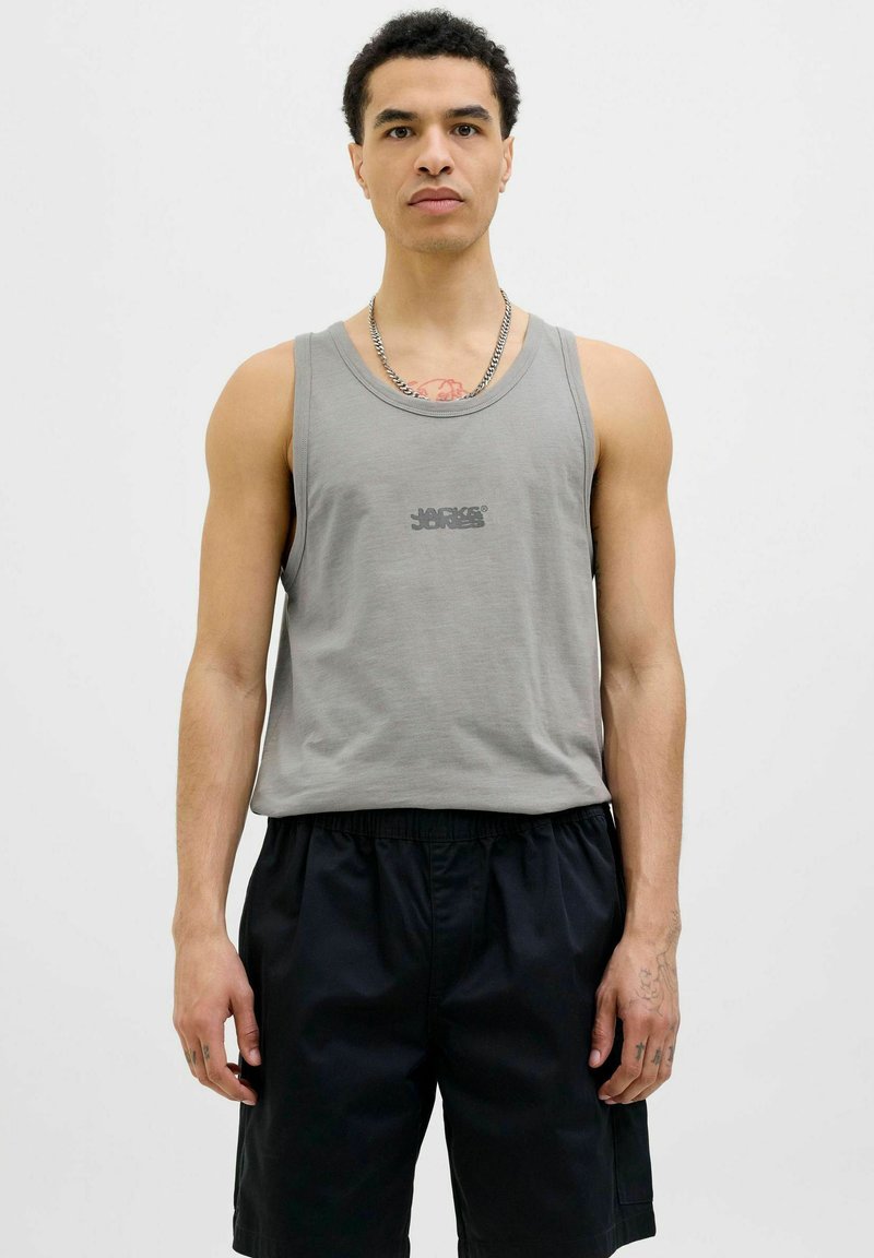 Camiseta de algodón gris sin mangas con cuello redondo y un pequeño logo negro centrado en el pecho, combinada con pantalones cortos negros. Textura suave.