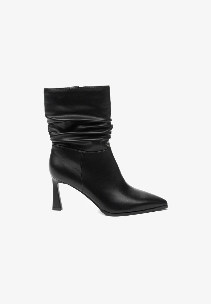 Bottine en cuir noir avec tige souple, bout pointu et talon haut stilettos. Texture lisse avec des détails de coutures minimaux.